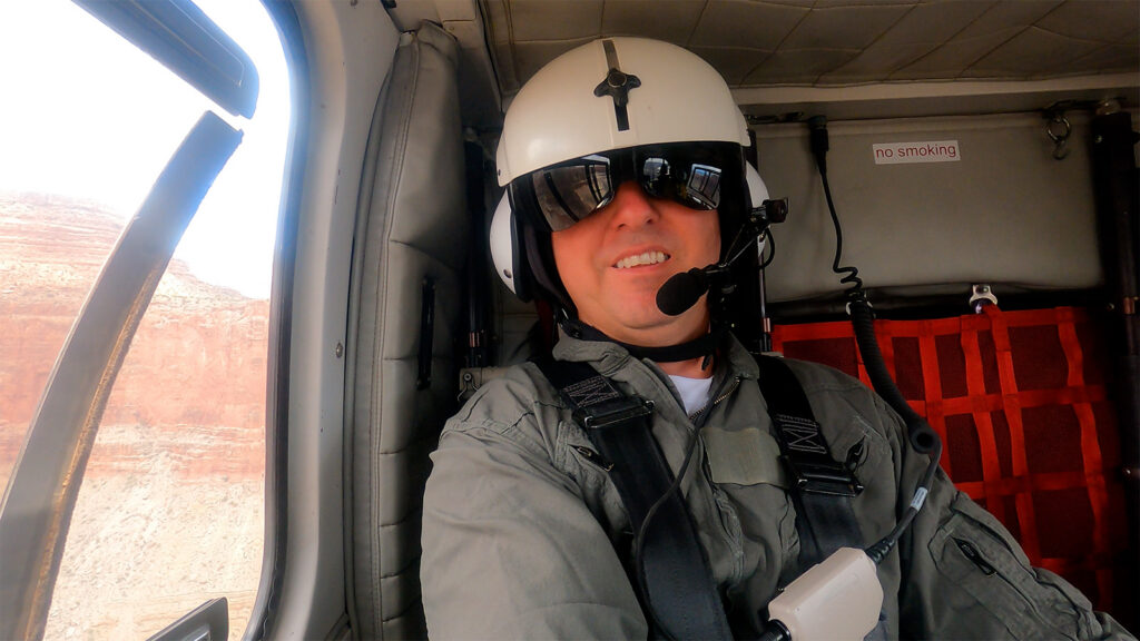 Carlos Femmer wearing a flight suit and aviation helmet inside a helicopter flying through the Grand Canyon.