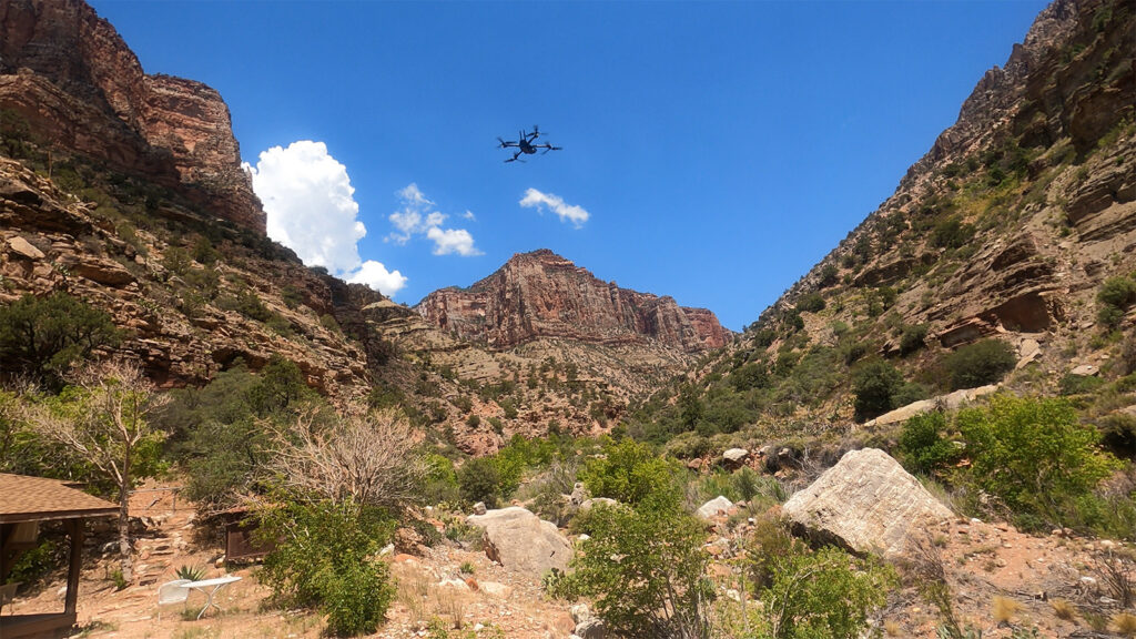 Skydio drone flying below the rim of the Grand Canyon between steep canyon walls under a clear blue sky.